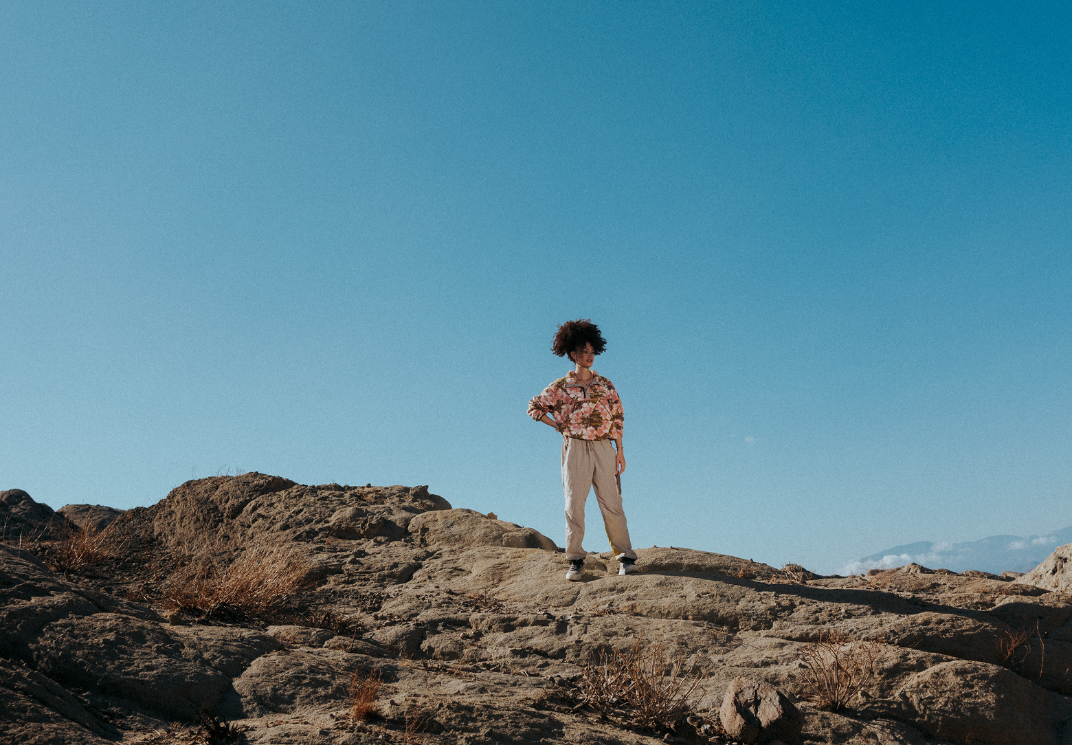 A woman standing on a rocky peak wearing hiking pants and a fleece.