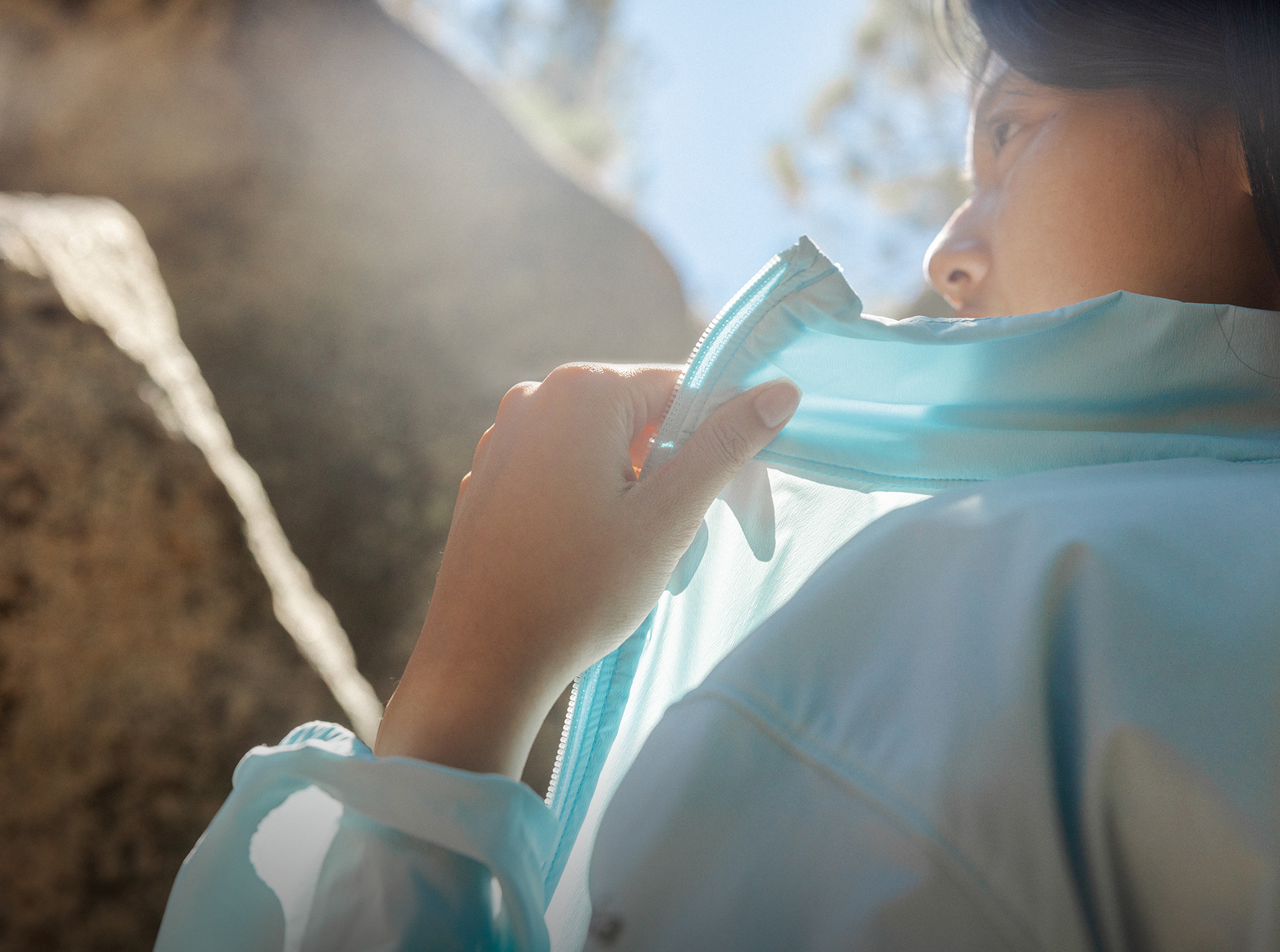 Close-up of a woman wearing a blue lightweight jacket in a sunny outdoor setting.