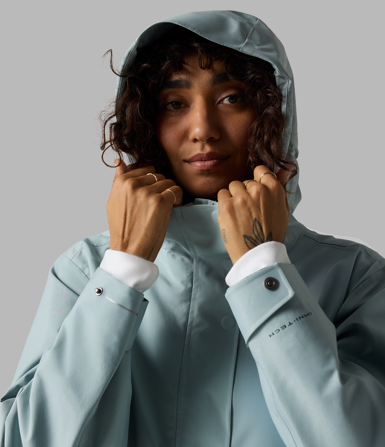 A woman wearing a blue jacket with the hood up against a grey background .