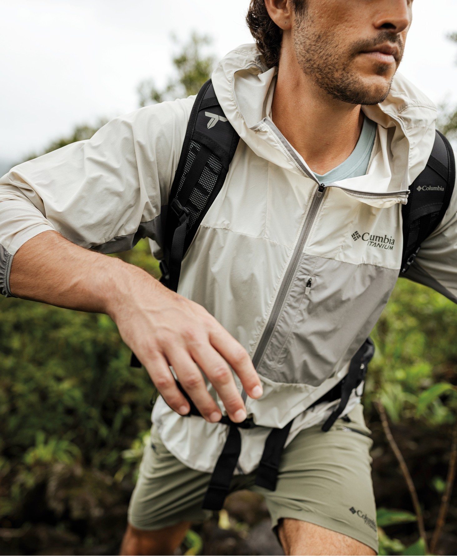 A man wearing a white jacket and black backpack, green shorts, hiking in a foggy landscape.