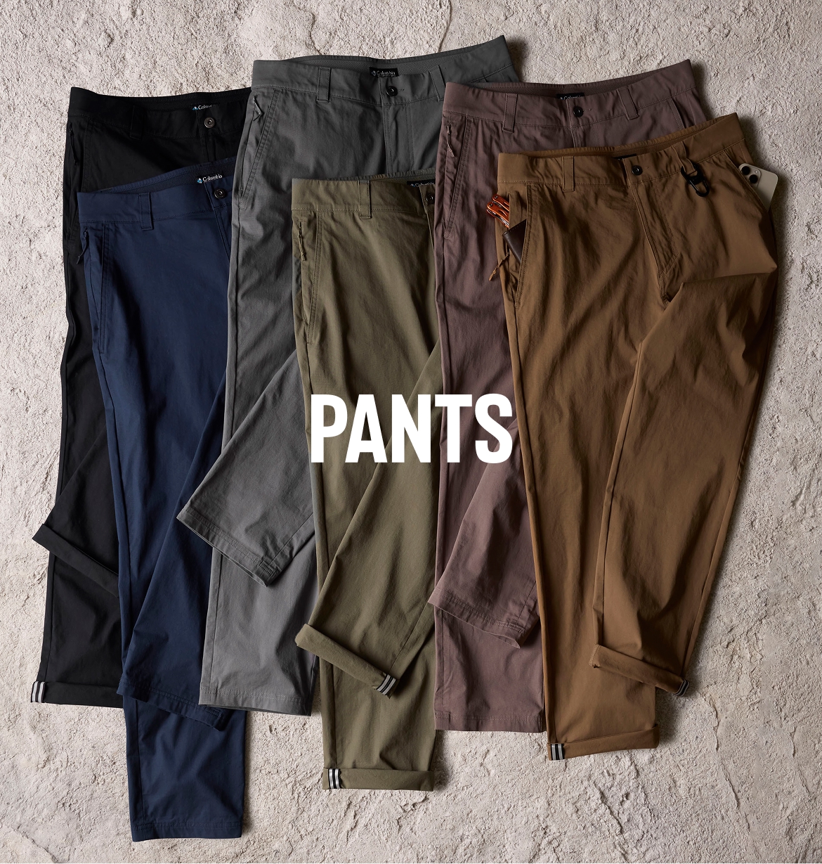 Six ROC pants laid on top of a rock texted background