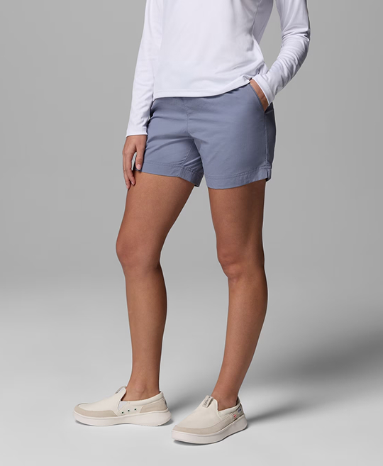 Waist-down image of a woman wearing blue shorts and tan slip-on shoes.