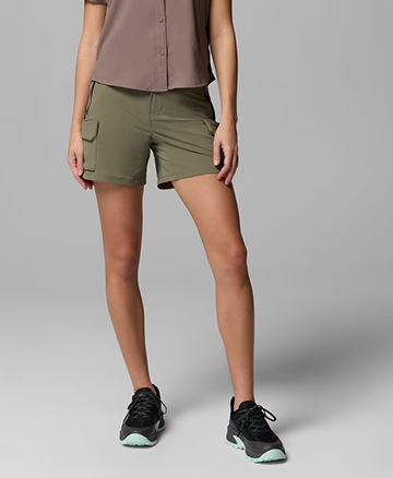 Waist-down image of a woman wearing green shorts and black sneakers.