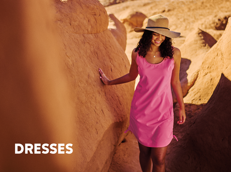A woman wearing a pink dress and sun hat in the desert, with text: DRESSES