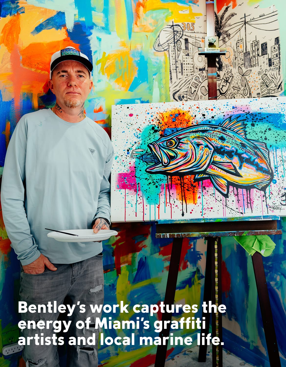 The artist Bentley standing next to a painting of a fish.