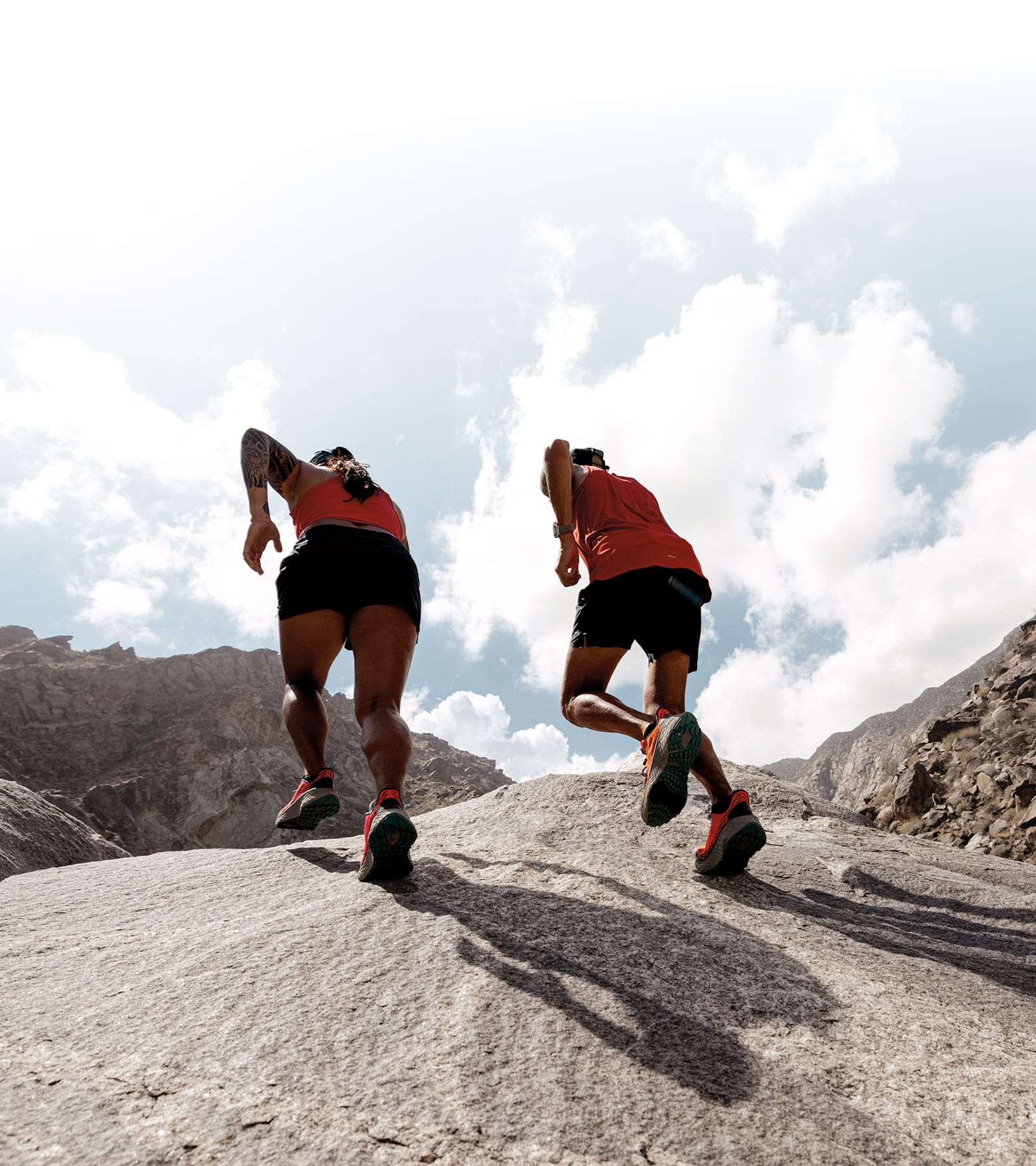 Two trail runners running over a boulder