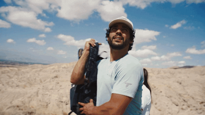 A gif of a man climbing up rocks to get to the top in an arid environment.