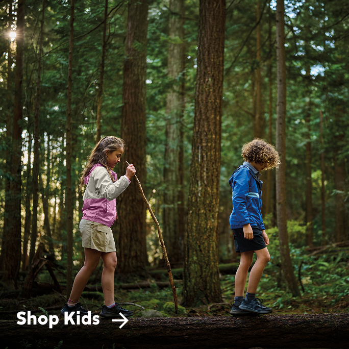 Two kids hiking a trail, little girl behind the boy has a hiking stick.