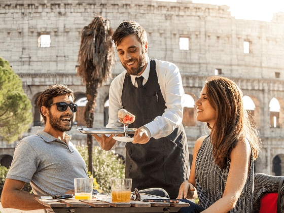 Couple being served gelato at a cafe in front of the Colosseum, in Italy.
