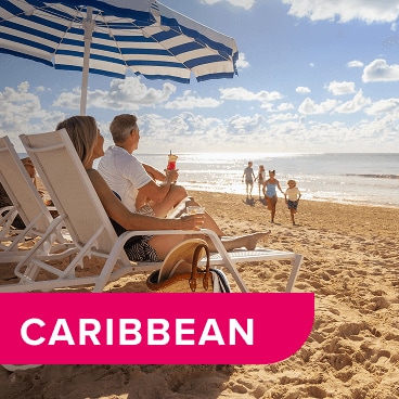 Couple relaxing in lounge chairs under an umbrella on the beach.