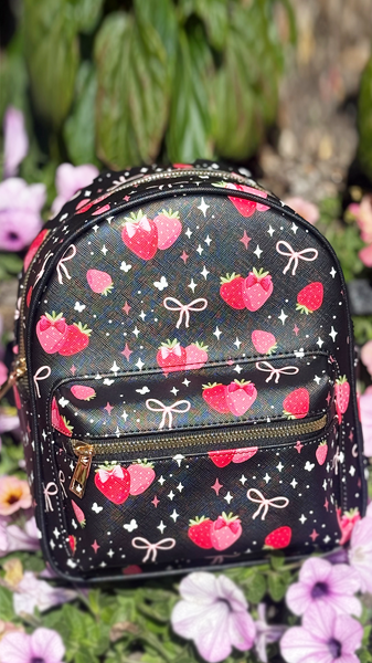 Black and pink strawberry and bows print mini backpack in garden. 