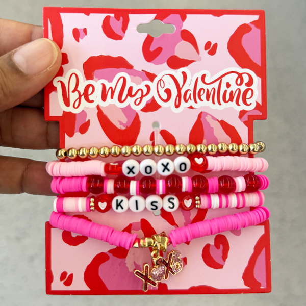 A pack of pink, red, and gold beaded bracelets, including letter beads spelling “XOXO” and “KISS,” displayed on pink and red Valentine-themed backing.