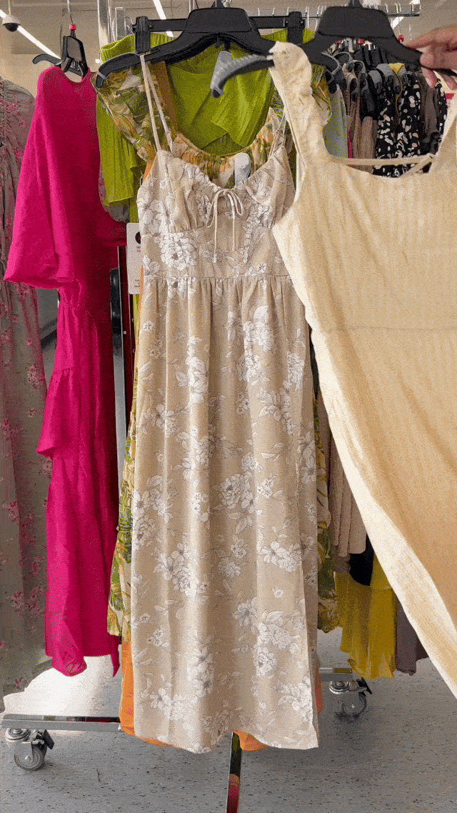 A soft floral midi dress styled for spring, surrounded by bright and patterned dresses on a rack.