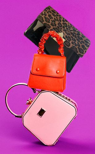 A styled stack of handbags featuring a small red top-handle bag, a black clutch with leopard print, and a pink structured handbag with a circular handle, set against a purple backdrop.