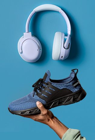 A pair of white over-ear headphones floats above a blue running shoe with black laces, which is being held in a hand against a solid blue backdrop.
