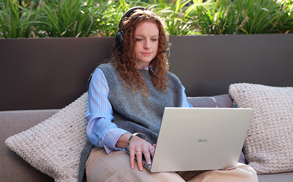 A woman sitting on an outdoor sofa with her Dell Pro Plus PB14250 