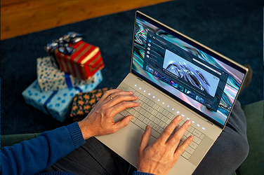 A person next to gift-wrapped boxes using their Dell laptop computer to generate greeting card text. 