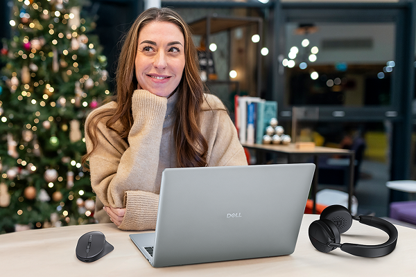 A woman sits at a table behind a Christmas tree with a Dell laptop, mouse and wireless headphones.