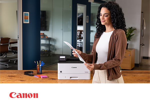 A person in a modern office admiring a document next to a Canon laser printer. 