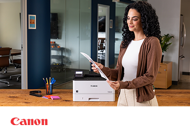 A person in a modern office admiring a document next to a Canon laser printer. 
