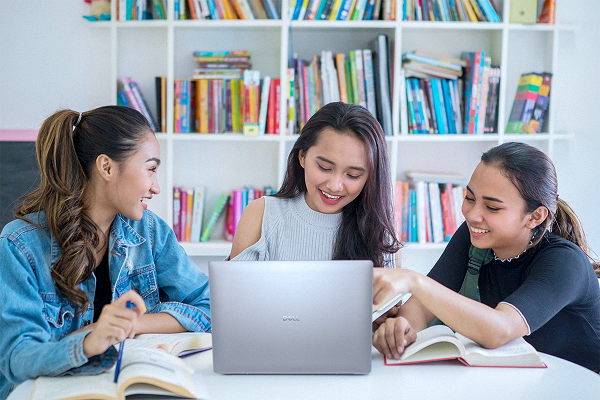 Three students enjoying collaborating on a school project around a Dell laptop computer.