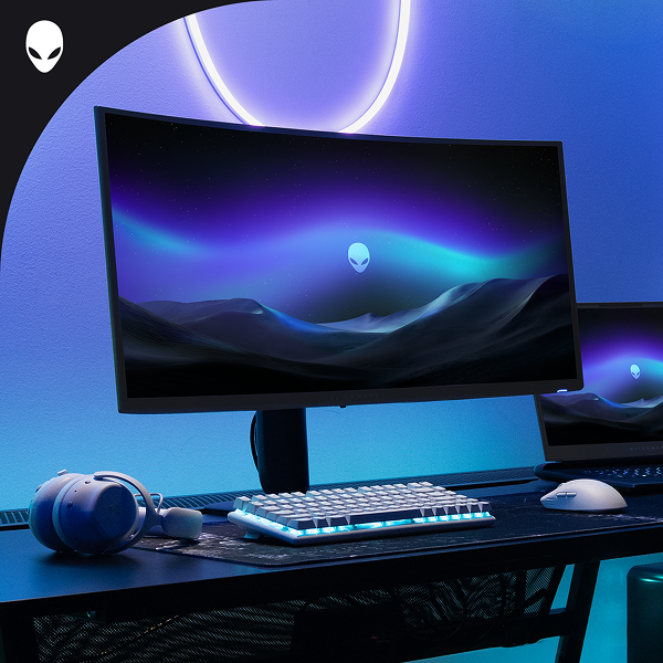 A dramatically-lit gaming setup with an Alienware monitor, laptop, wireless keyboard and mouse.