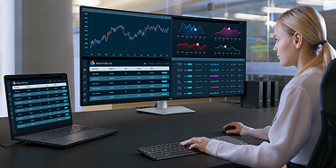 An office worker tracking the status of recent orders across multiple dashboards on a widescreen Dell UltraSharp 52 TBT monitor, laptop, wireless keyboard and mouse.