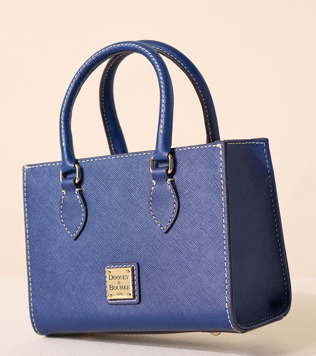 The Saffiano Janine 20 offers a compact, structured interior that holds just the essentials in an organized way. It comfortably fits a small bifold or compact continental wallet, smartphone, keys on the interior key hook, and a slim sunglasses sleeve, with space left for a small hand cream, lip color, and travel-sized sanitizer. The inside zip pocket secures valuables such as cash or jewelry, while the slip pocket keeps cards, transit passes, or receipts within easy reach, so everything stays tidy and accessible during your day or evening out. This petite shoulder bag is ideal when you want to travel light without sacrificing polish. Carry it by the top handle for a refined, ladylike look at dinners, events, or brunch dates, or attach the adjustable strap to wear it as a hands-free shoulder or crossbody companion for shopping, sightseeing, or commuting. Its tailored silhouette pairs effortlessly with dresses, structured suiting, or casual denim, making it a versatile choice for occasions when you need a sleek accent rather than a full-size carryall.