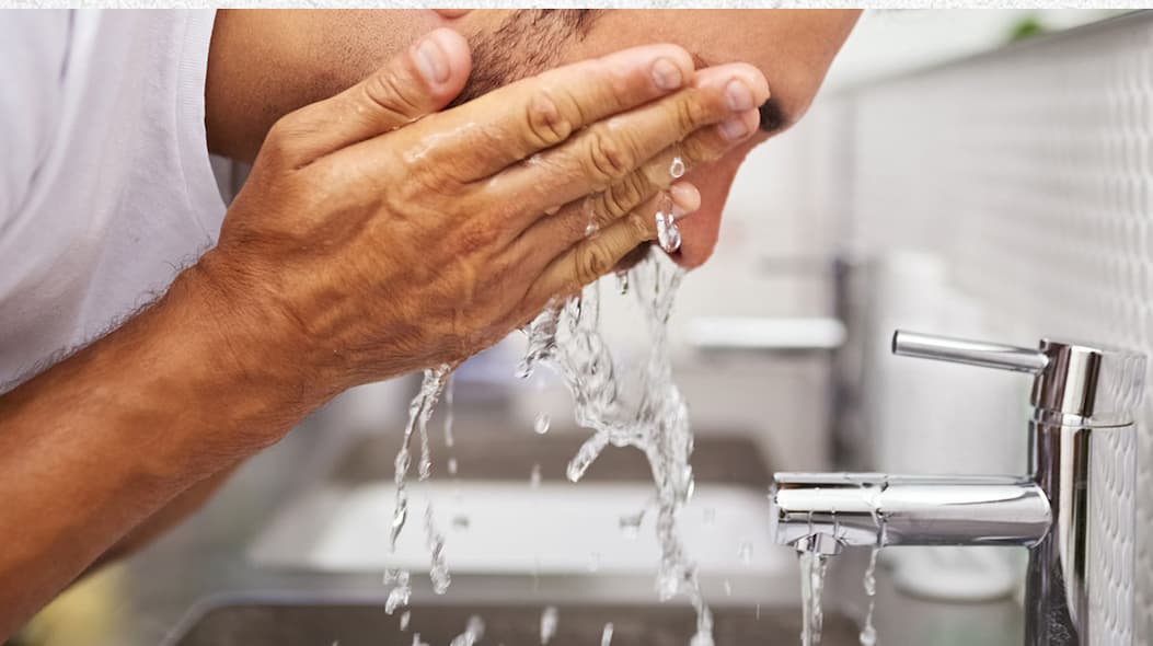 Man cleaning his face in a sink.