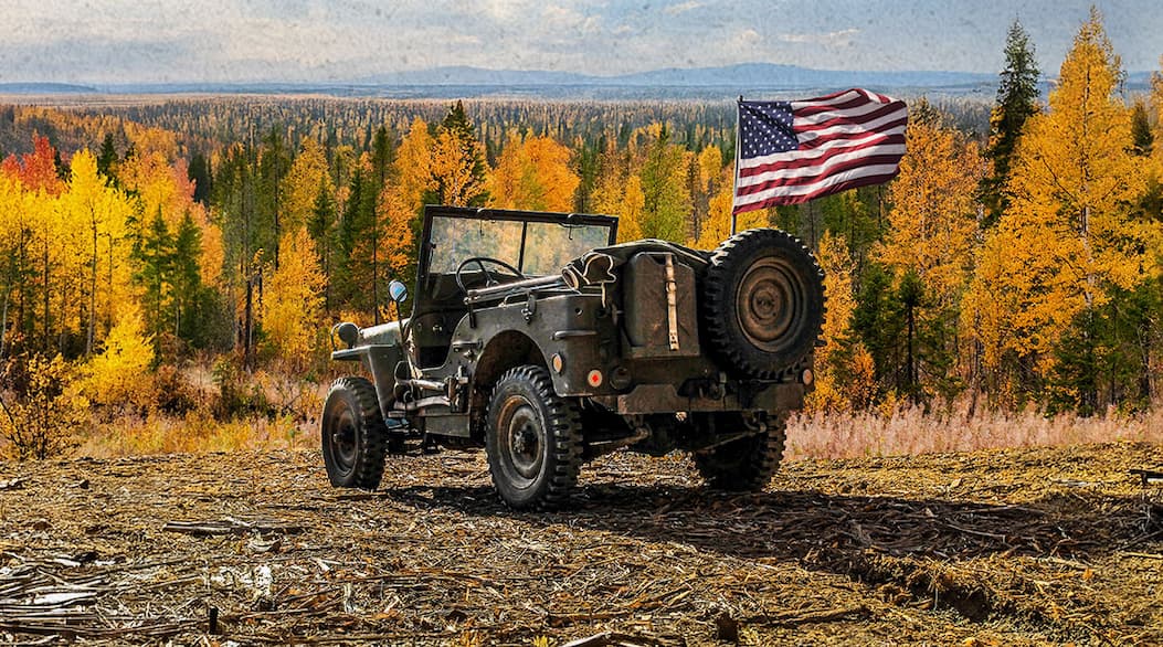 Jeep with an american flag looking out at a forest background.