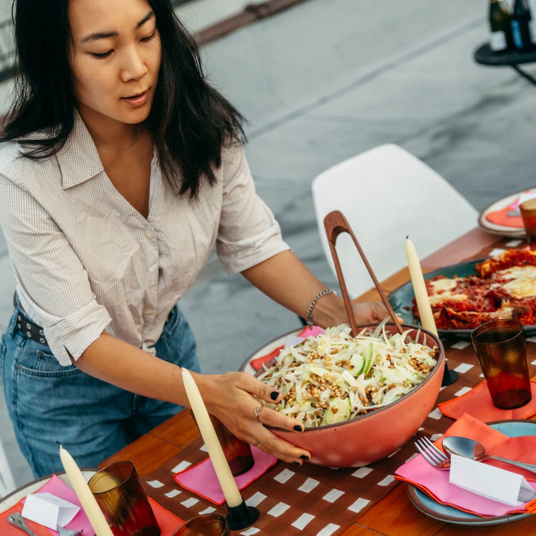 A women places a Mixing Bowl in Guava with a fennel salad in it onto a brightly style table.