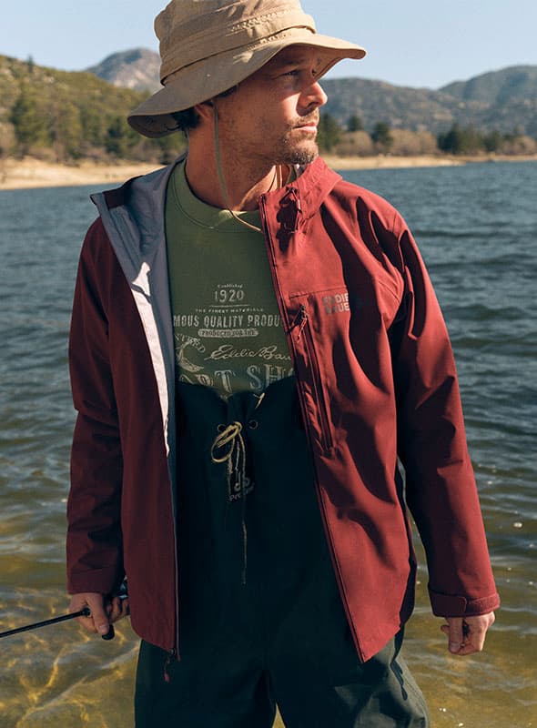 Man wearing maroon rain jacket and standing in river.