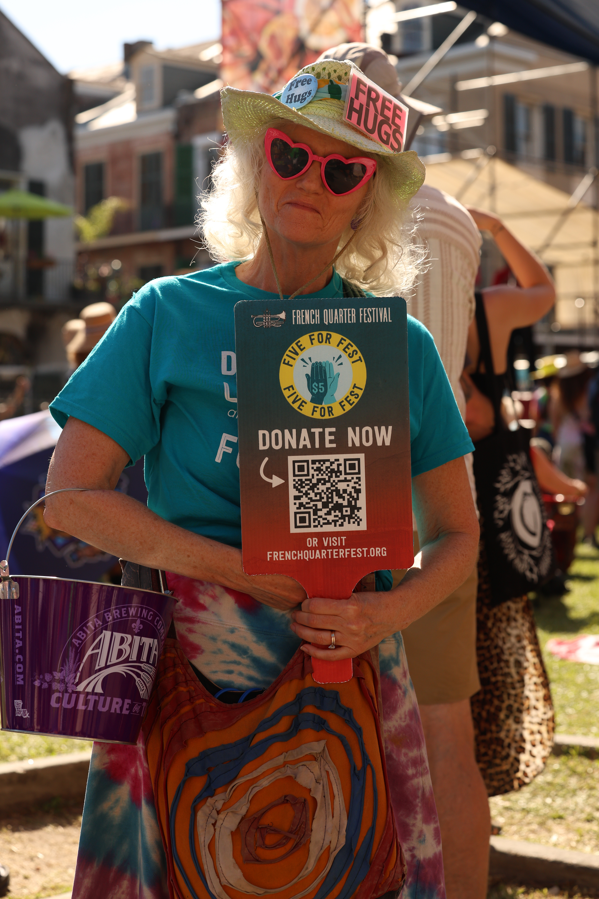 a woman wearing a hat and sunglasses holding a donate now sign