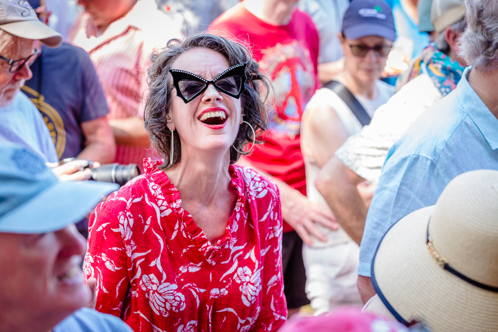 a woman in a red dress and sunglasses laughing in a crowd of people