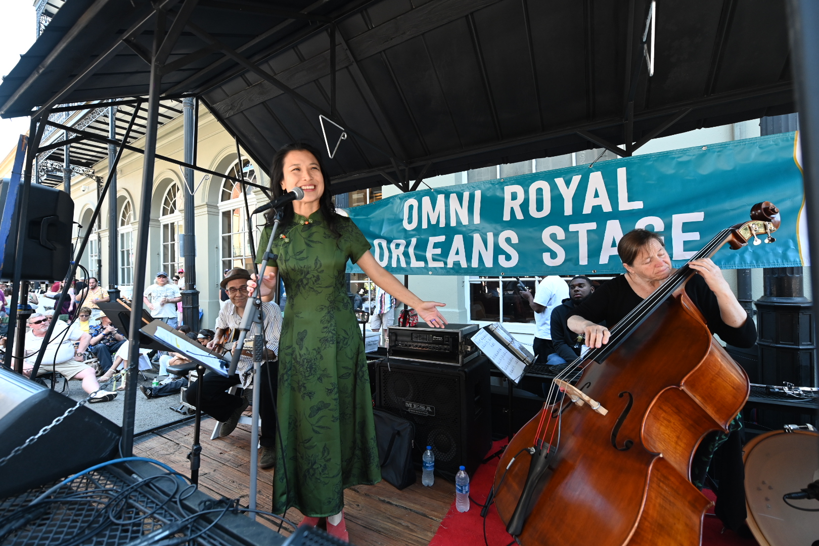 a woman in a green dress standing on a stage next to a cello player