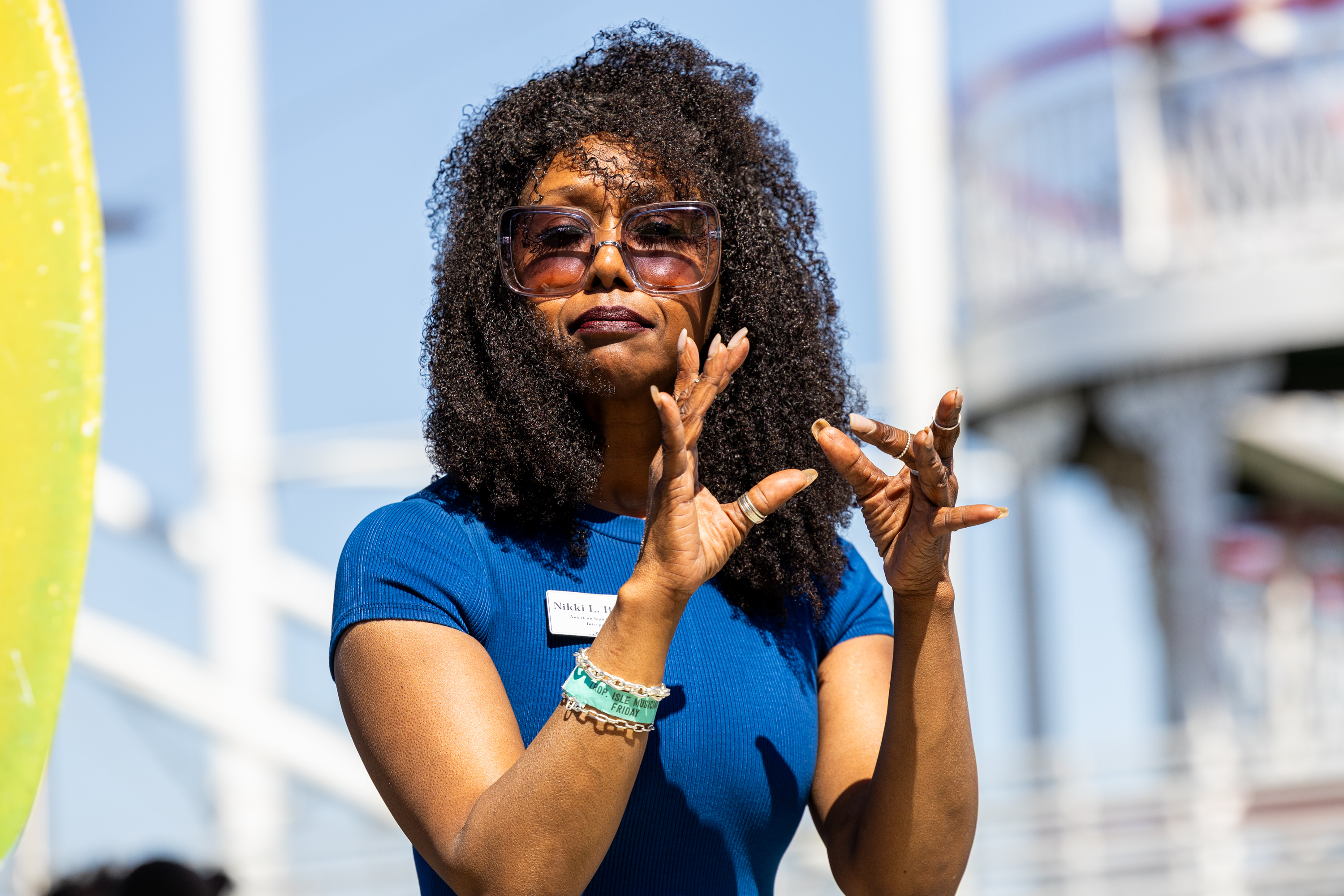 a woman in a blue shirt and sunglasses gestures with her hands