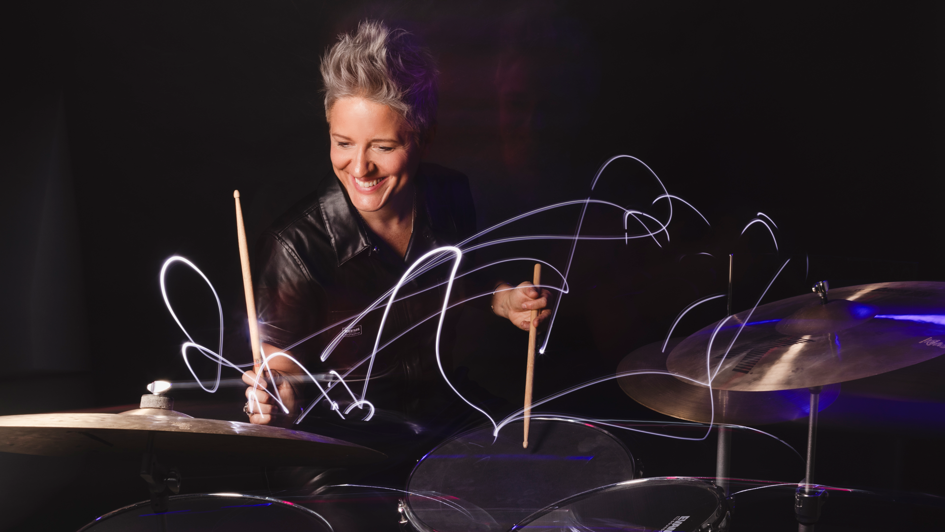 Allison Miller playing a drum set in a dark room