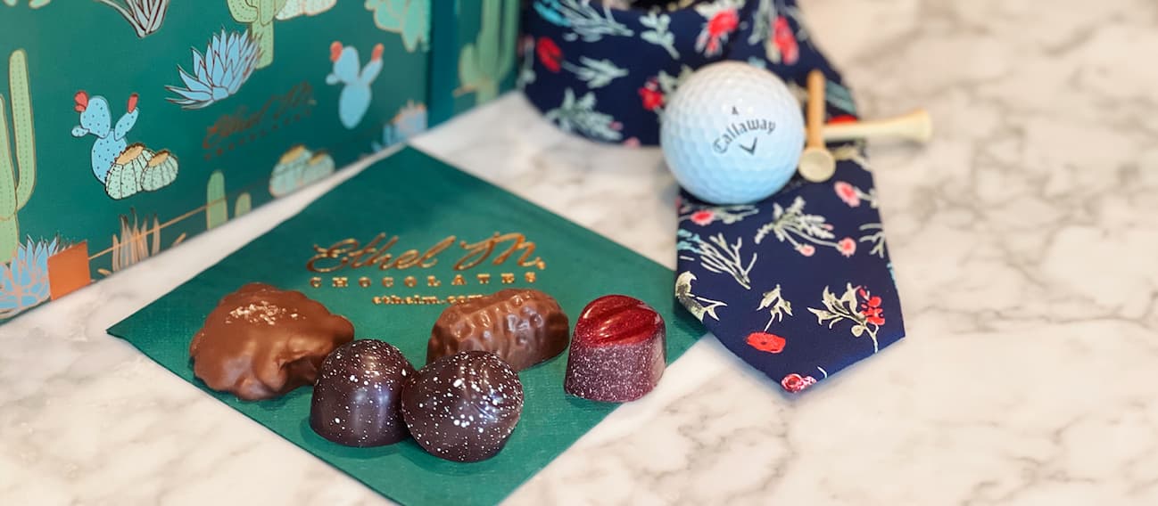 Ethel M Chocolates gems on a Ethel M Chocolates napkin next to a tie and golf ball.