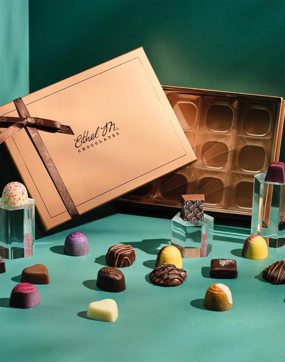 Ethel M Chocolates Copper Custom Chocolate Box with a variety of Ethel M Chocolate gems surrounding it.