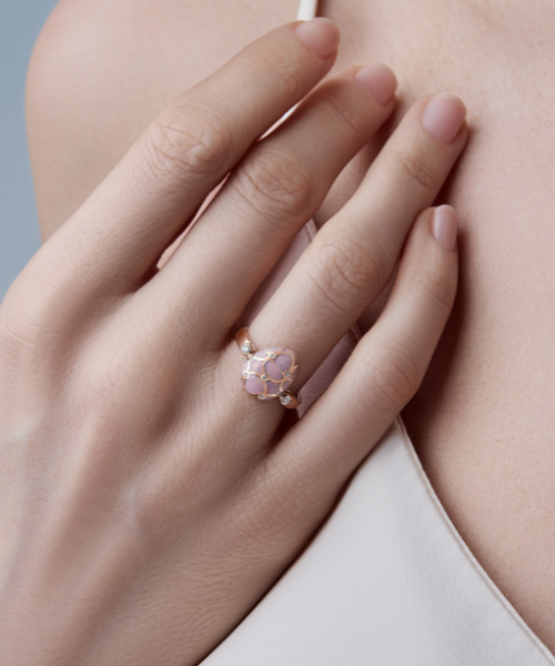 Close-up of a hand wearing a rose gold Fabergé ring featuring a pink guilloché enamelled egg motif.