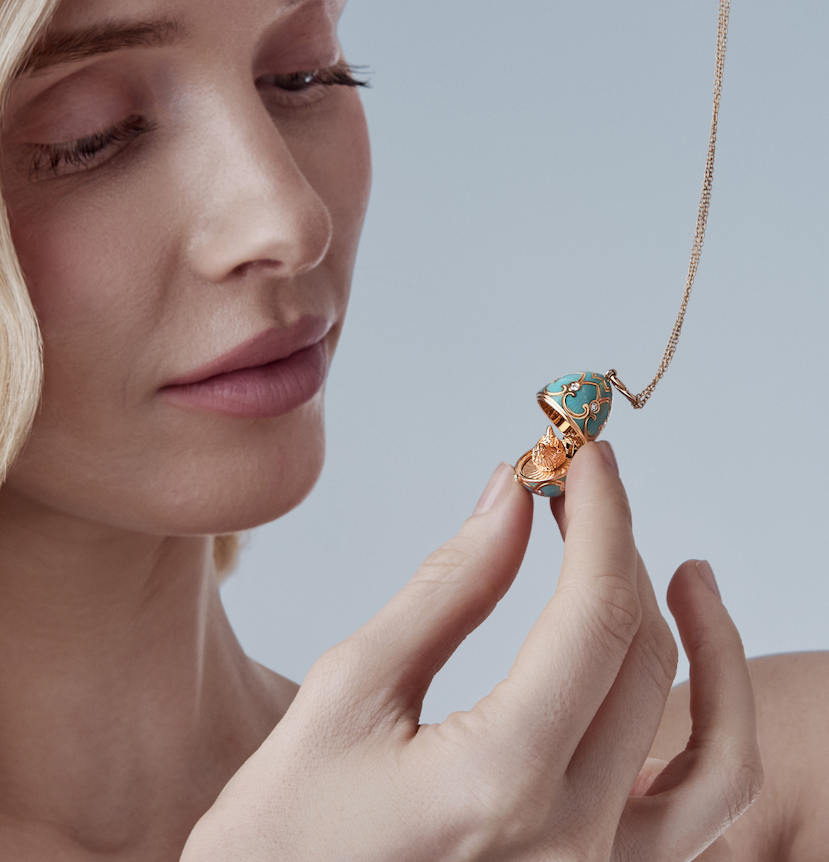 Side profile of a model holding an open turquoise and gold Fabergé egg pendant, revealing a tiny hand-sculpted gold hen inside