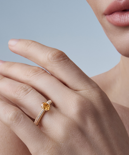 Close-up of a model's hand wearing an 18k fluted gold ring set with a central yellow sapphire gemstone and accent diamonds