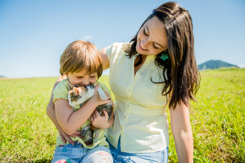 Mom with child sitting in a field with a little kitten