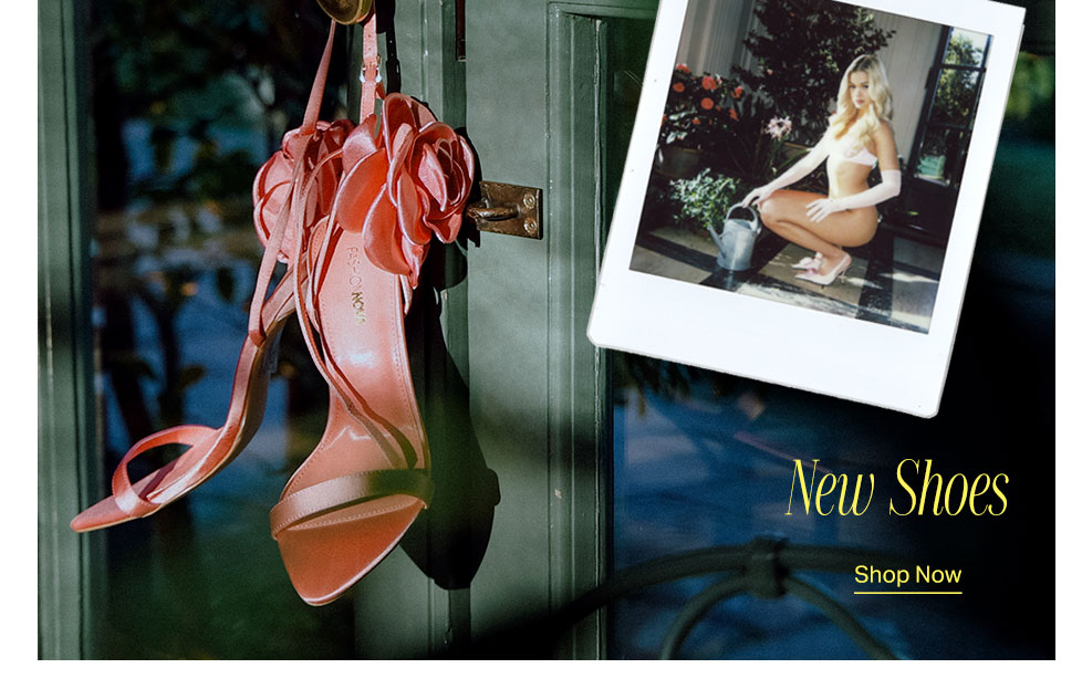Pink satin floral heels hanging on a dark door, next to a polaroid of a model wearing similar shoes. Explore our New Shoes collection. Shop Now!