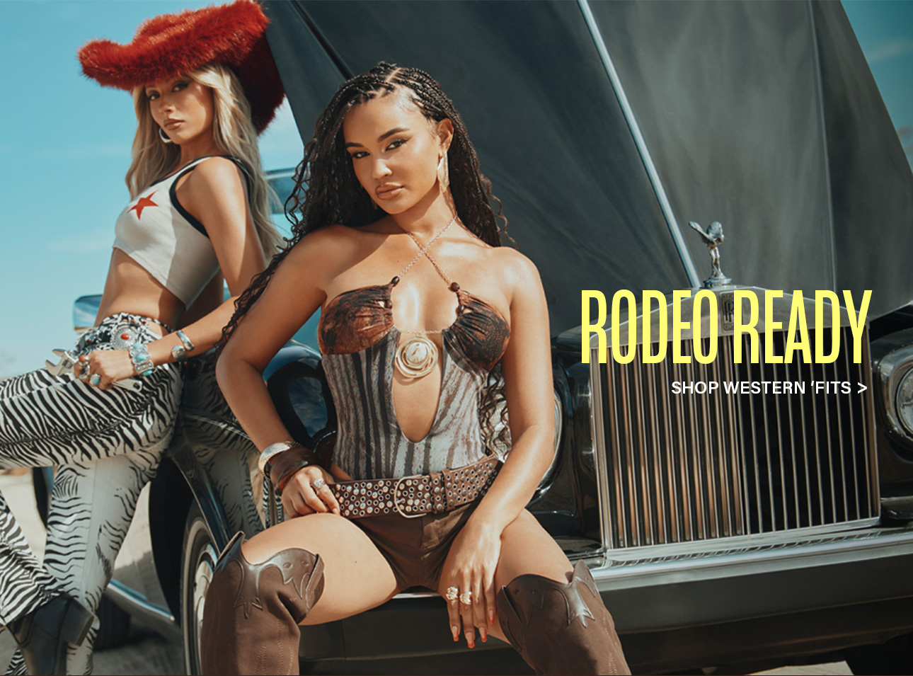 Two models rock rodeo-ready western fashion: a red fuzzy hat, zebra print pants, a corset top, and cowboy boots, posed by a classic car. Shop western fits.