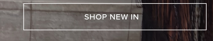 White "SHOP NEW IN" button on a blurred background featuring a grey textured wall and dark flowing hair. Discover the latest fashion arrivals.