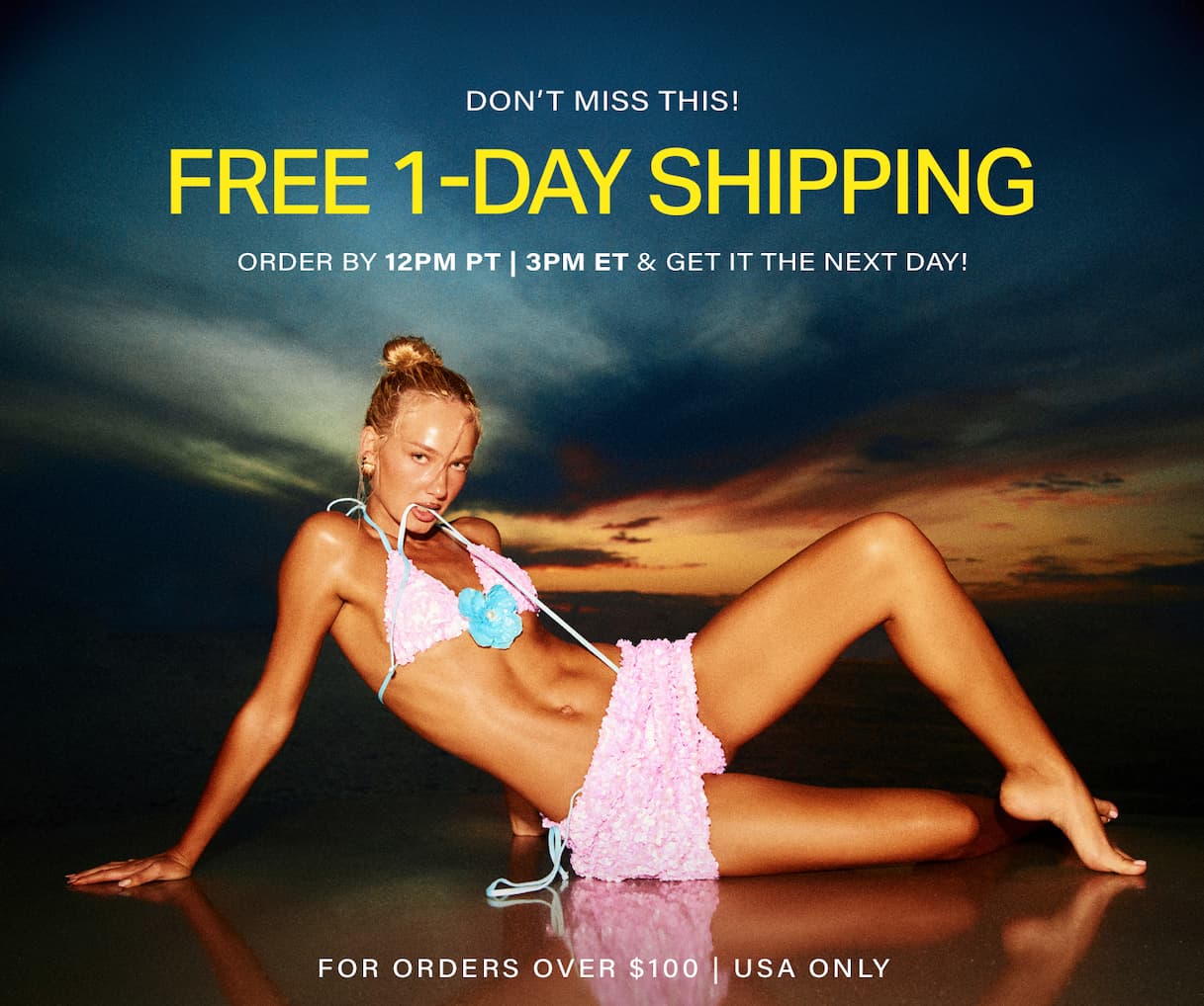 Model in a ruffled pink bikini with a blue flower reclines on a reflective shore at sunset. Get free 1-day shipping on new swimwear.