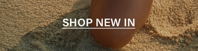 Text 'SHOP NEW IN' over golden sand and warm-toned skin. Explore our new arrivals and latest fashion collection now.