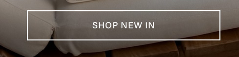 "SHOP NEW IN" button centered on a soft taupe sofa, highlighting new arrivals and encouraging discovery of the latest collection.