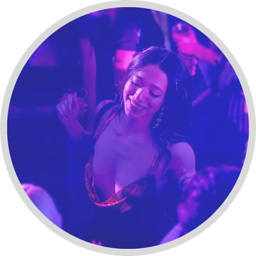 Image of a Anora wearing a red dress dancing in a club with purple and pink light from the movie ANORA